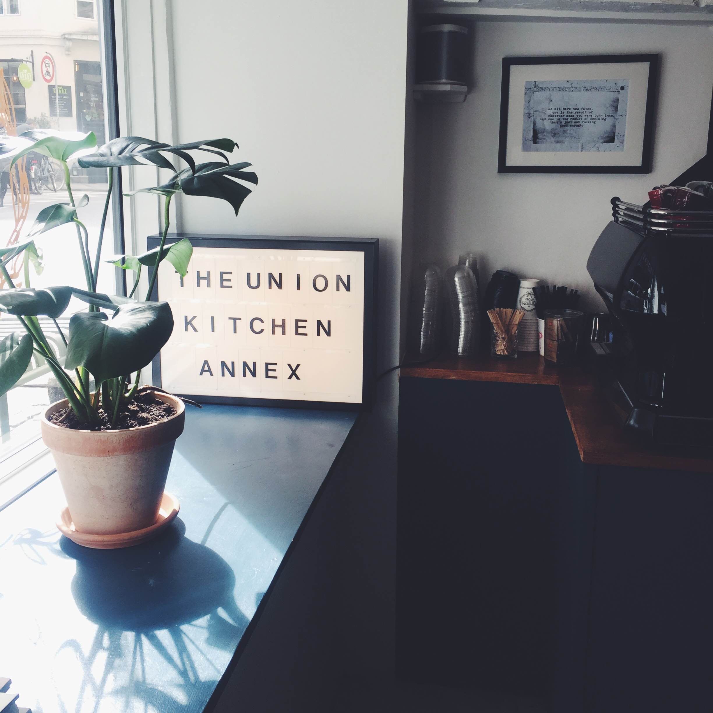 Indretning på The Union Kitchen Annex café i København. Plante, skilt og kaffebar
